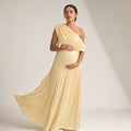 Model wearing Rowan asymmetric one-shoulder maternity maxi dress in apricot, showing bump-skimming silhouette and diagonal neckline