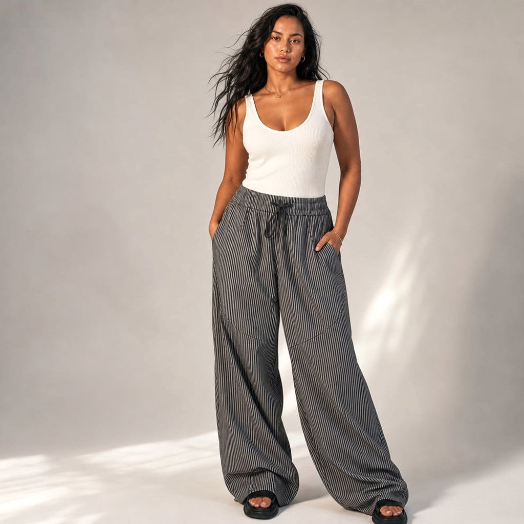 Model wearing grey barrel-leg trousers with a tucked blouse, showing the full arc of the wide leg from hip to hem