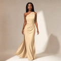 Model wearing a light brown asymmetrical maxi dress with one side sweeping the floor and a raised slit hem on the opposite side.